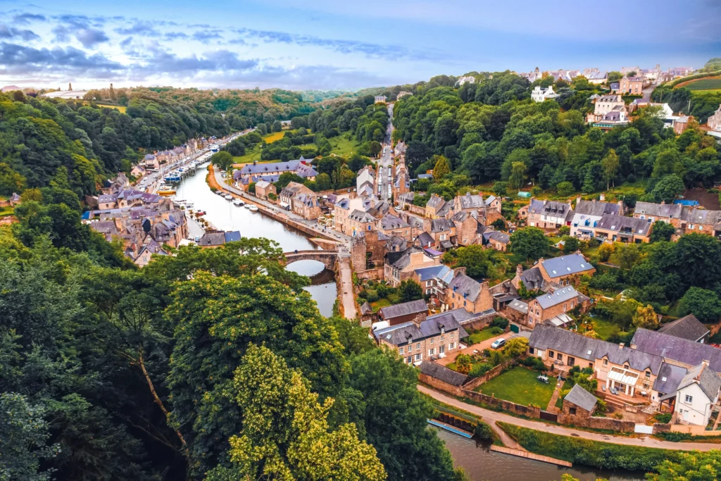 Vue aérienne du port de Dinan entouré de maisons en pierre et de verdure, illustrant le charme médiéval de la Bretagne dans les circuits MJ Prestige.